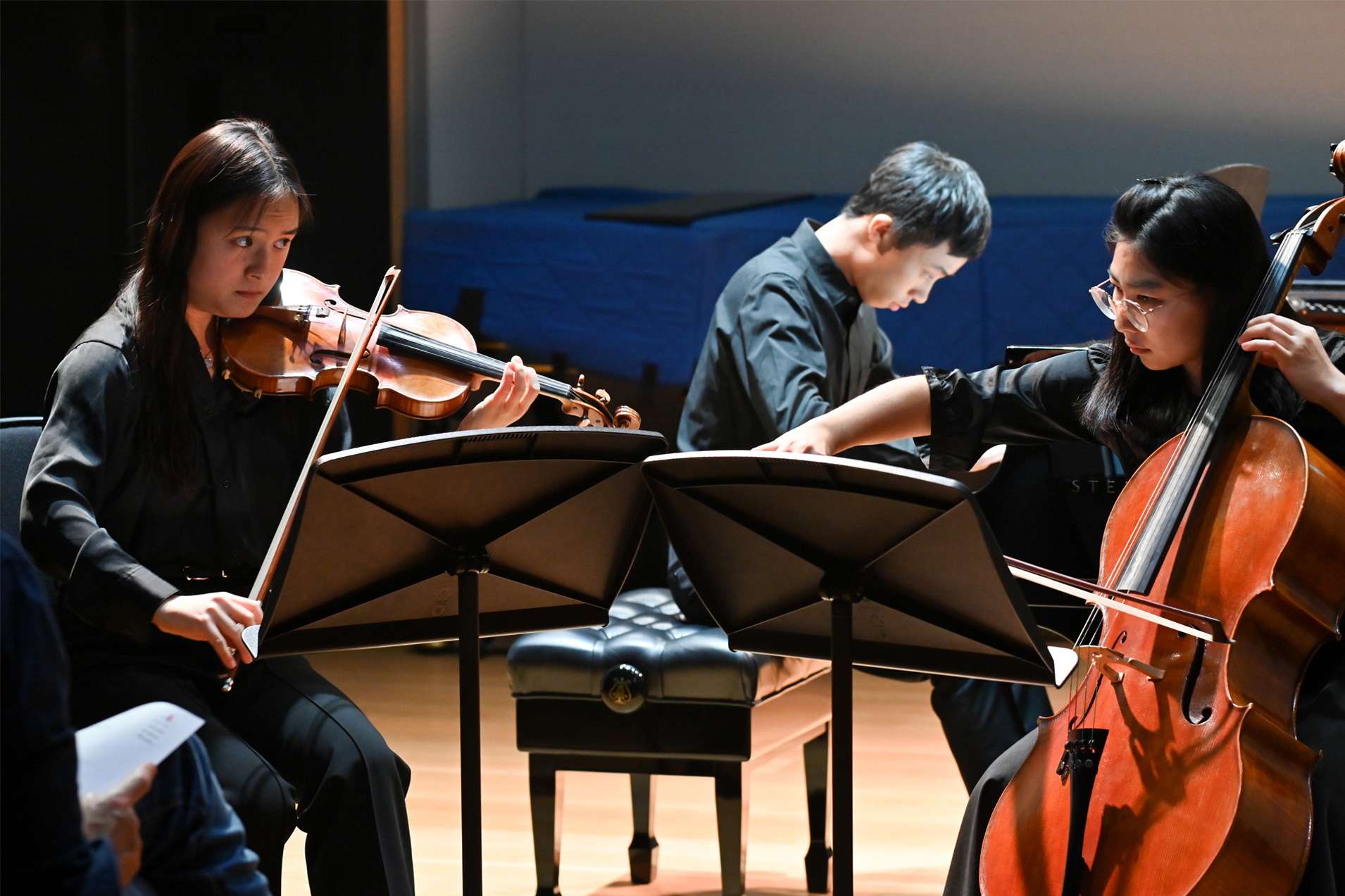 Students performing in a string quartet at a chamber concert, wearing smart black attire, performing the piano, violin and cello.